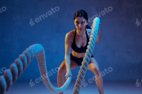 Caucasian young female athlete practicing on blue studio background in neon light