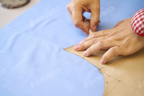 Preview: Dressmaker traces a pattern on a blue fabric with chalk