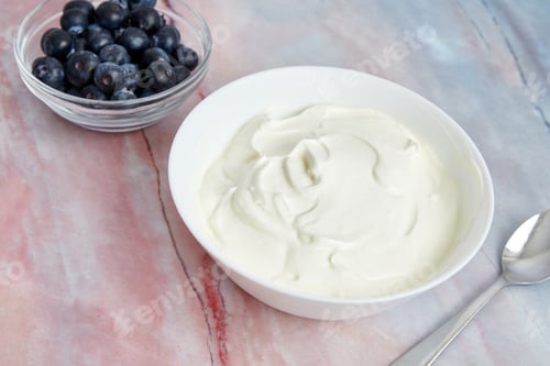 Preview: Closeup of a bowl with yogurt, blueberries served with spoon on a table