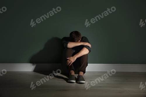 Preview: Depressed young man sitting on floor in darkness