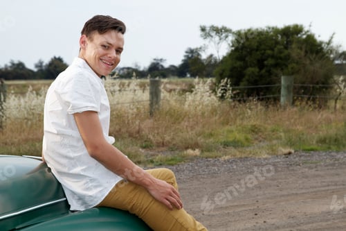 Preview: Portrait of young man sitting on bonnet of vintage morris minor