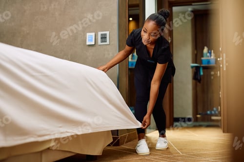 Preview: African American hotel maid making bed in guest's room.
