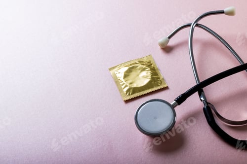 Preview: High angle view of condom in pack with stethoscope against pink background, copy space