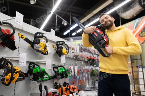 Preview: satisfied and happy customer hugging a petrol saw in a gardening equipment store