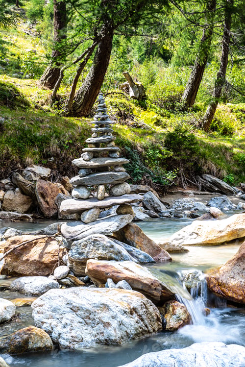 Preview: Tower made of small stones by the creek surrounded by lush greenery. Val Poschiavo, Switzerland.