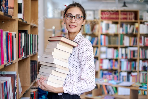 Preview: Young woman with a stack of books in library