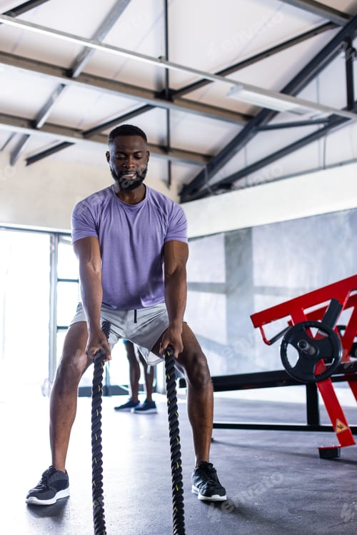 Preview: African American young male athlete training with heavy ropes in gym