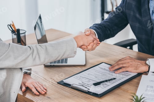 Preview: cropped view of shaking hands businessman and woman over table in office, compensation concept