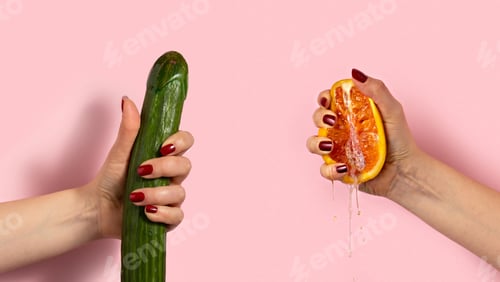 Preview: Female hand with half of juicy orange and cucumber on pink background. Sex concept.