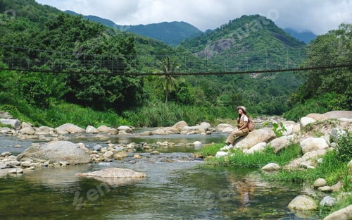 Preview: A woman sitting on the rock by the creek with forest and mountain views