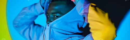 Preview: handsome bearded man putting on hood in colorful digital projector lights, fashion concept, banner