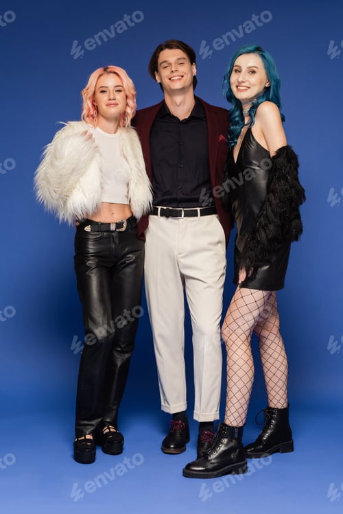 Preview: full length of queer friends in faux fur jackets near nonbinary person in white pants on blue