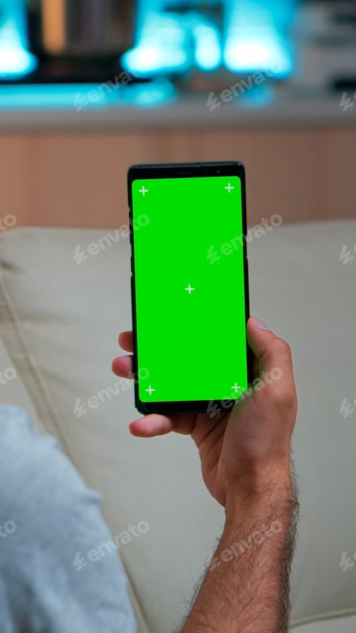 Preview: Relaxed man looking at smartphone with mock up green screen chroma key display