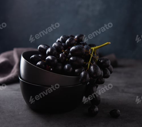 Preview: a cluster of juicy black grapes lies in a dark gray bowl on a dark gray table