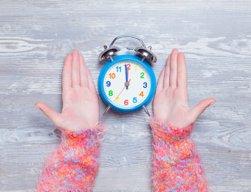 Preview: Female hands holding clock on a table.