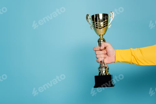Preview: cropped view of man holding golden trophy on blue