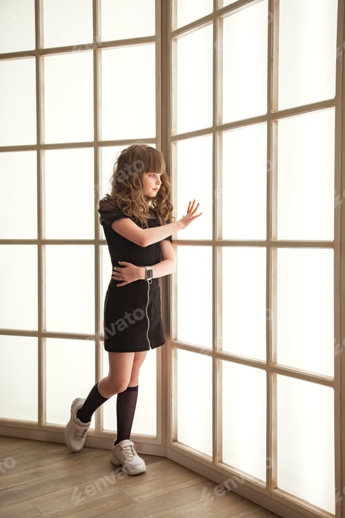 Preview: Sad image pensive teen girl in stylish black dress posing full length near window