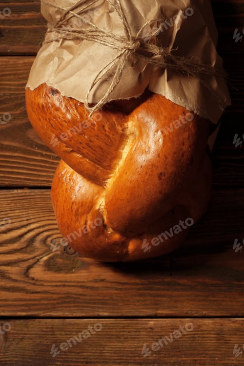 Preview: Freshly baked bread wrapped in paper on a wooden table on a sunny afternoon