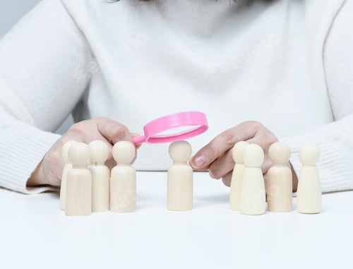 Preview: Woman holding a magnifying glass and wooden men on a white table.