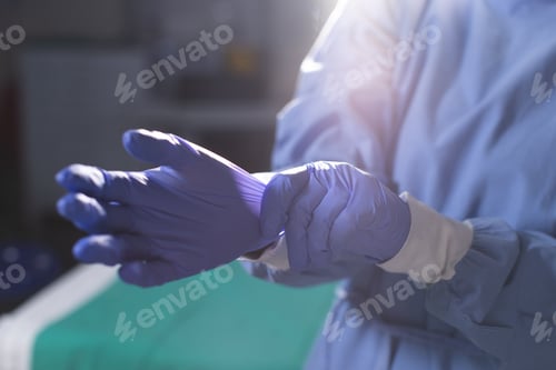 Preview: Midsection of biracial female surgeon wearing surgical gown and medical gloves in operating theatre