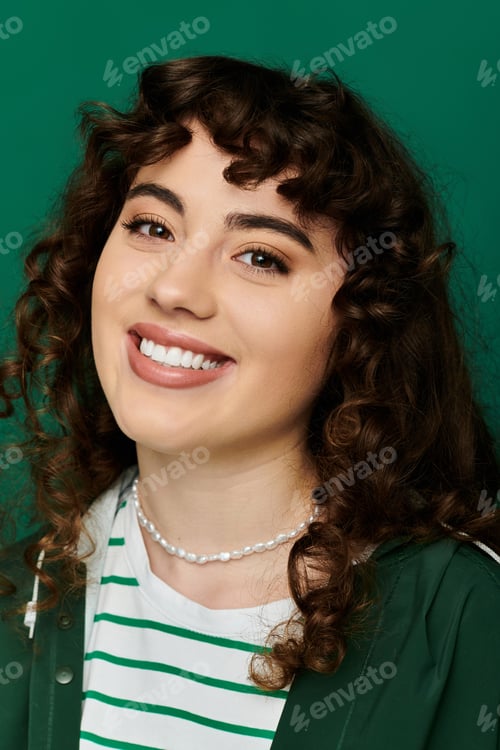 Preview: Stylish young woman with curly hair expressing joy against a vibrant green backdrop