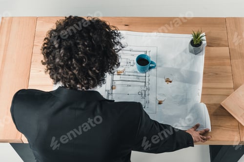 Preview: rear view of businessman working with blueprints at workplace in office