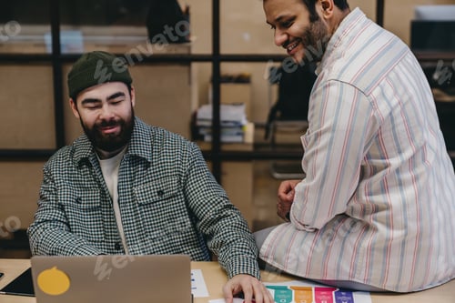 Preview: Positive multiethnic bearded male coworkers working on project with laptop
