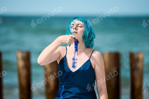 Preview: Artistic blue-haired woman performance artist in dress smeared with blue gouache paints on her body