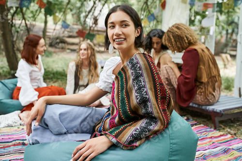 Preview: young smiling woman sitting on bean bag near blurred multiethnic friends in retreat center
