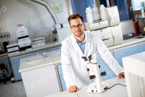 Preview: Young scientist in white lab coat working with binocular microscope in the material science lab