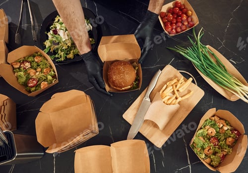 Preview: Prepared burger and vegetables. French fries. Man is packing food into the paper eco boxes