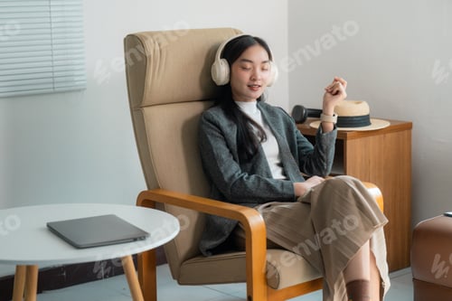 Preview: Young Asian businesswoman relaxing listening to music with headphones in armchair at home
