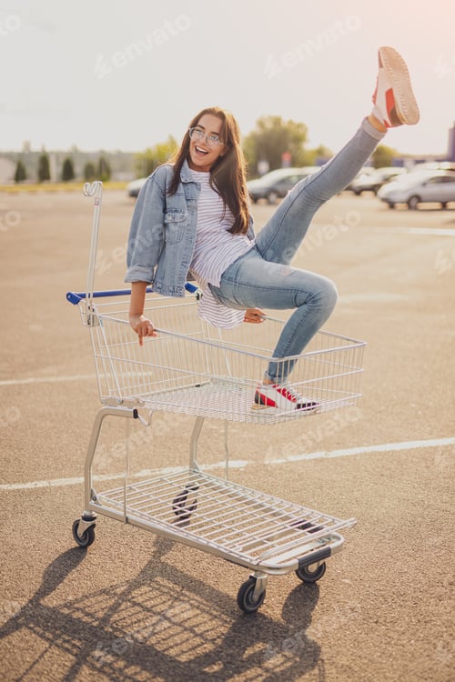 Preview: Excited young lady having fun on shopping trolley
