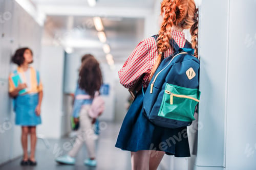 Preview: redhead schoolgirl with backpack in school corridor leaning on wall