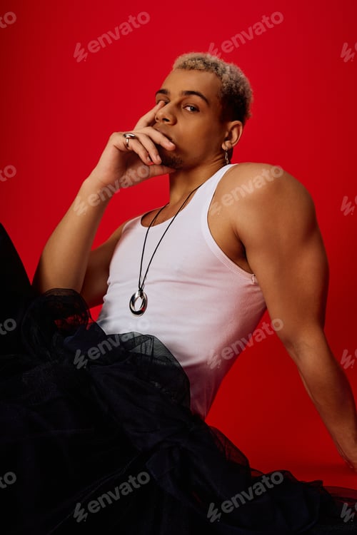Preview: Young man in stylish tank top poses against vibrant red studio backdrop