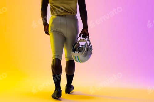 Preview: Midsection of african american male american football player with neon purple and yellow lighting