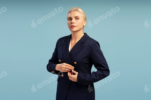 Preview: Elegant businesswoman buttoning her blazer on blue background