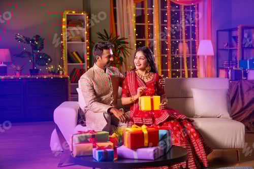 Preview: Indian young couple posing with gift boxes on diwali festival evening at home