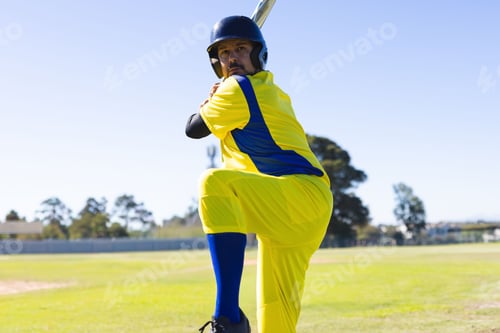 Preview: Mature male cricketer standing on cricket ground holding bat wearing yellow kit and helmet