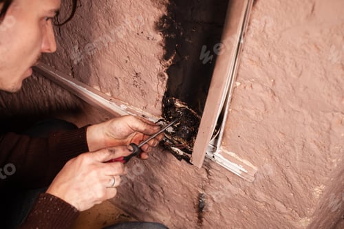 Preview: A man fixes a burnt socket. Short circuit, burnt wires. traces of smoke fire on the wall. The