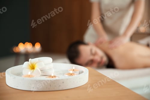 Preview: Composition with candles and blurred man receiving massage in spa salon. Space for text