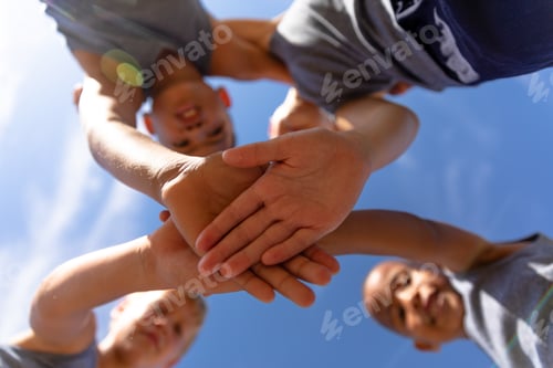 Preview: Directly below shot of multiracial elementary schoolboys stacking hands during soccer match