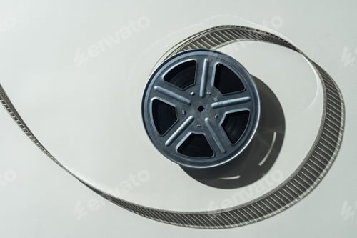 Preview: top view of film reel with twisted cinema tape on grey background
