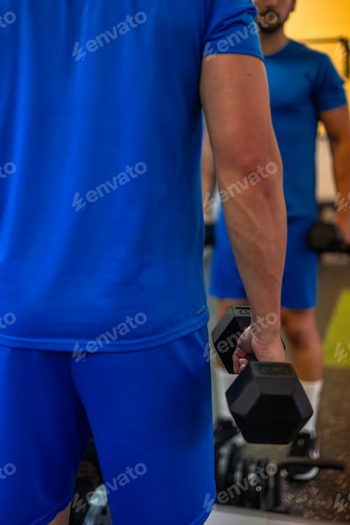 Preview: closeup of fitness sportsman's arm holding dumbbell for bicep exercises reflecting in gym mirror