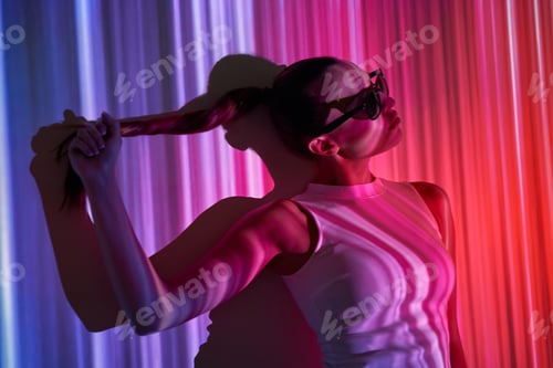 Preview: Attractive young woman in eyeglasses leaning at the wall with colorful lighting