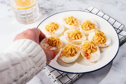 Preview: stuffed eggs with paprika, on a plate, a woman's hand reaches for it,