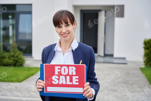 Preview: Young woman stands near country house with for sale sign