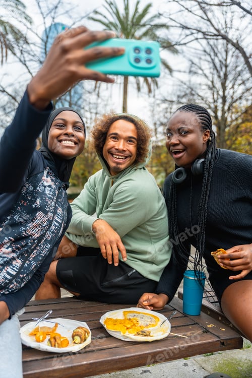 Preview: Diverse friends capturing group selfie during urban picnic