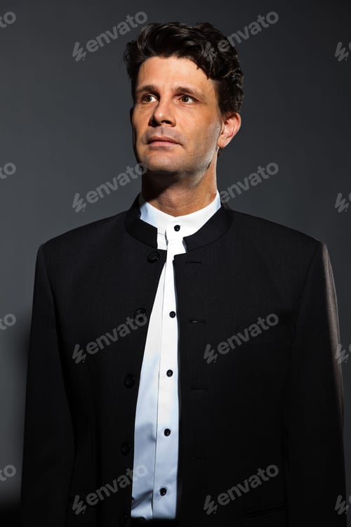 Preview: Wise Man In Black Costume With White Shirt Isolated On Dark Background. Studio Portrait.