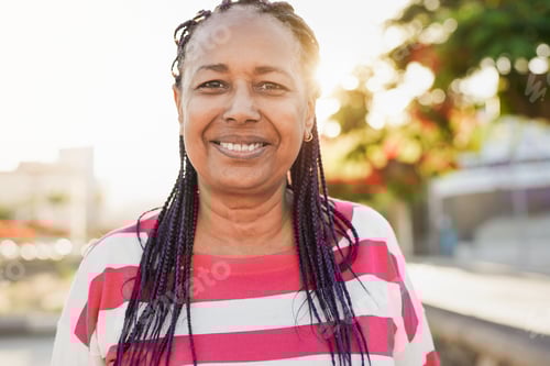 Preview: Mature african woman smiling on camera in the city with sunset in the background